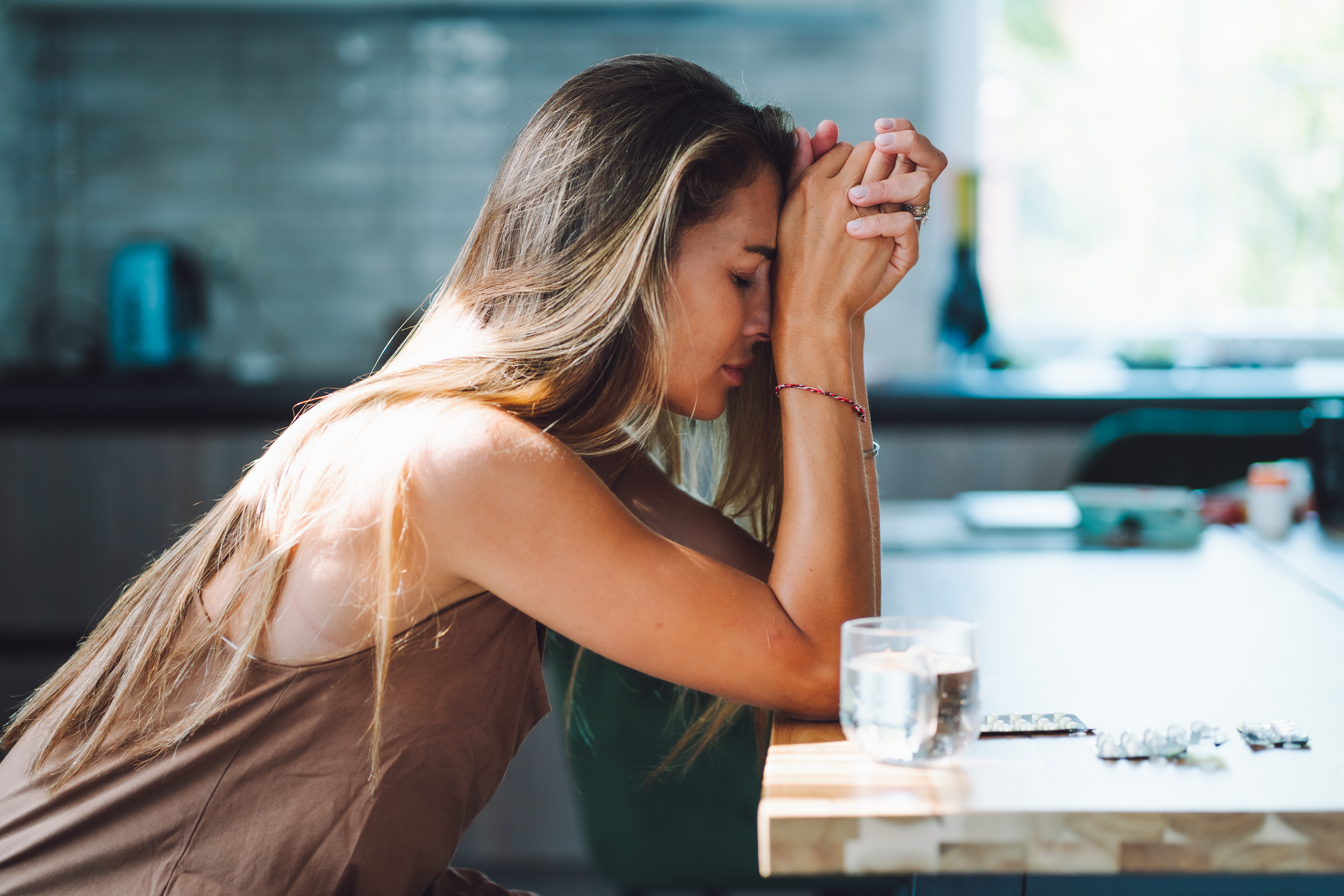 Domestic violence and women mental illness. Crying woman with head in hands drinking pills on the kitchen | Source: Getty Images