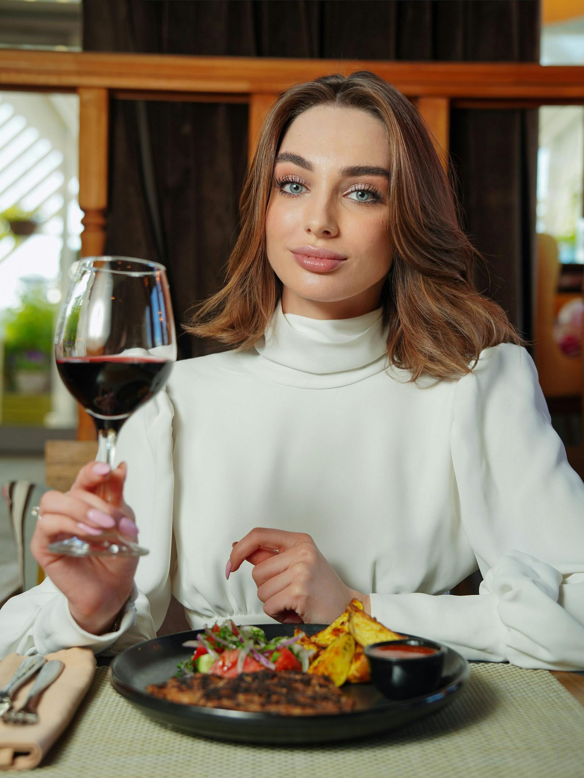 A woman sitting at a dinner table holding a glass of red wine | Source: Pexels